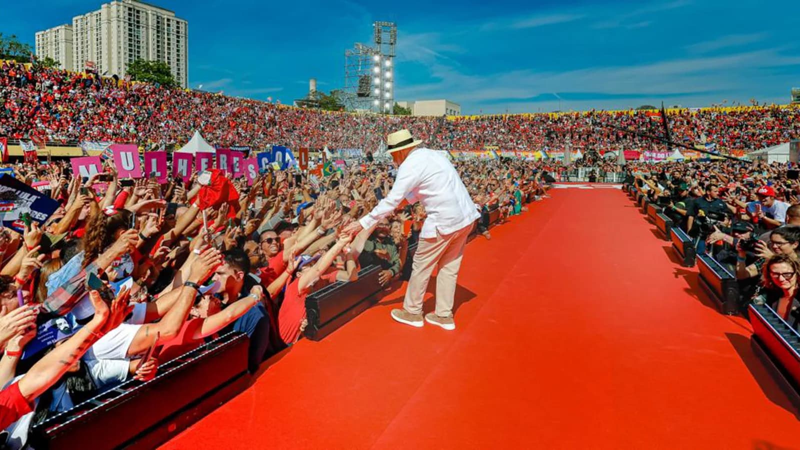Lula, de branco e chapéu, acena para multidão em tapete vermelho no lançamento da campanha
