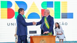Lula aperta a mão do ministro Wellington Dias em cerimônia no Palácio do Planalto, com painel escrito Brasil ao fundo