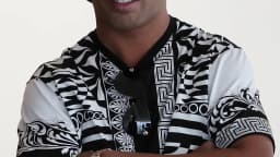 Ronaldinho Gaúcho de braços cruzados, usando boné preto e camisa estampada