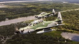Dois caças A-29 Super Tucano da Força Aérea Brasileira voando lado a lado sobre área de floresta e rio, em imagem de arquivo
