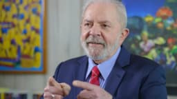 Lula gesticula durante discurso, com pintura ao fundo