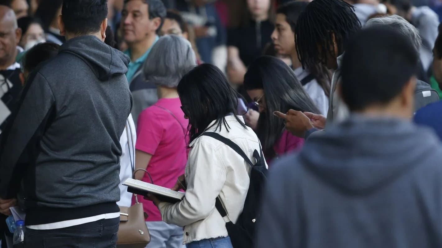 Fila de candidatos aguardando para fazer prova de concurso público, um deles consultando anotações
