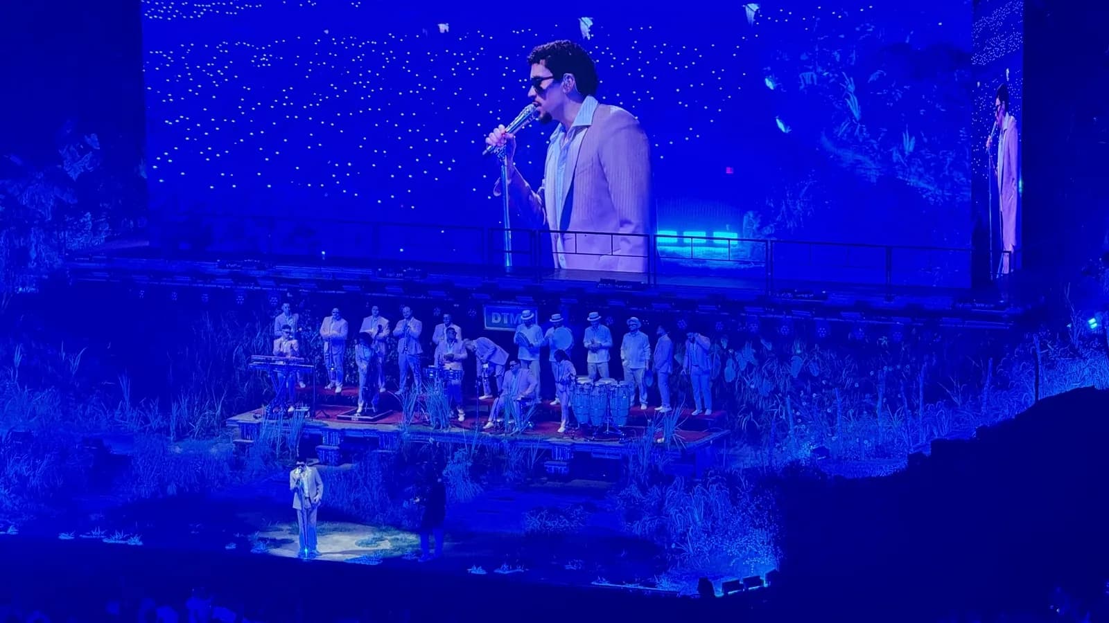 Bad Bunny se apresenta em show, com banda ao fundo e iluminação azul