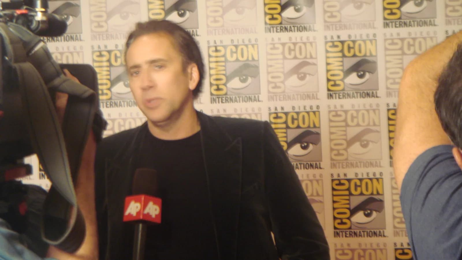 Nicolas Cage em evento de Comic-Con, diante de microfones