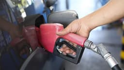 Mão de frentista segurando bico de bomba de combustível para abastecer veículo em posto de gasolina