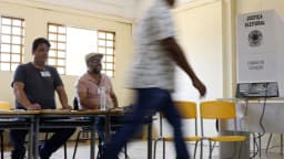 Eleitor caminha para votar em seção eleitoral com mesários ao fundo