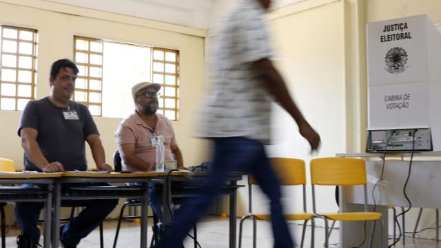 Eleitor caminha para votar em seção eleitoral com mesários ao fundo