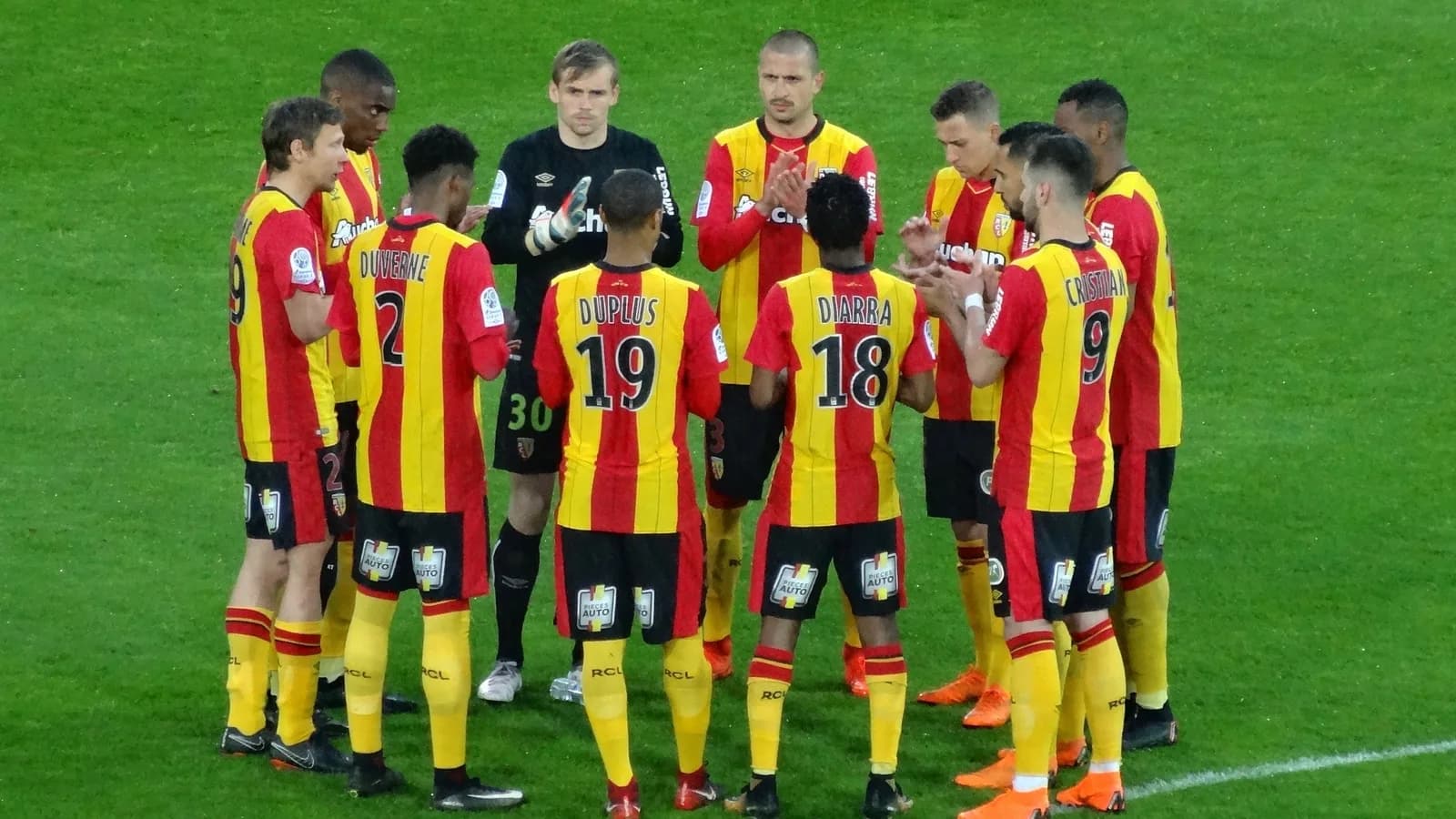 Jogadores do RC Lens reunidos em campo, com o uniforme listrado vermelho e amarelo do clube (imagem de arquivo)