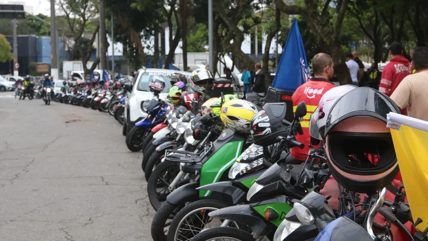 Motociclistas de aplicativo enfileirados com motos estacionadas