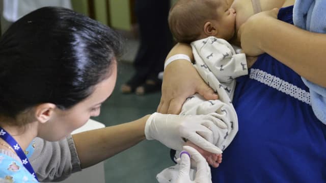 Profissional de saúde aplica vacina em bebê recém-nascido no colo da mãe