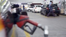 Frentista caminha entre veículos para abastecer carro em posto de combustível