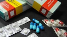 Caixas de remédio com aviso de venda sob prescrição médica e cartelas de comprimidos e cápsulas sobre superfície escura