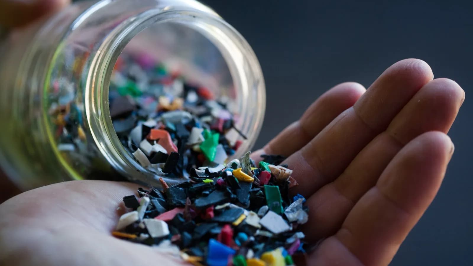 Mão segura resina plástica reciclada em fragmentos coloridos, foto ilustrativa do setor petroquímico