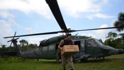 Militar carrega caixa de urna eletrônica próximo a helicóptero durante apoio logístico a eleições