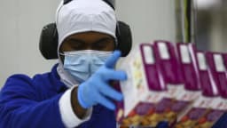 Trabalhador com máscara, luvas e protetor auricular manuseia produtos em linha de produção