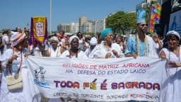 Grupo de pessoas de religiões de matriz africana em marcha, segurando faixa com os dizeres 'Toda fé é sagrada'