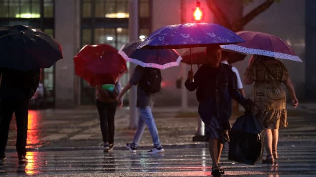 Pessoas andam com guarda-chuvas em dia de chuva na cidade, à noite
