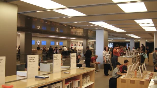 Interior de uma loja da Apple com clientes analisando produtos em mesas de exposição