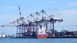 Navio porta-contêineres atracado sob guindastes portuários no Porto de Santos, com pátio de contêineres ao fundo