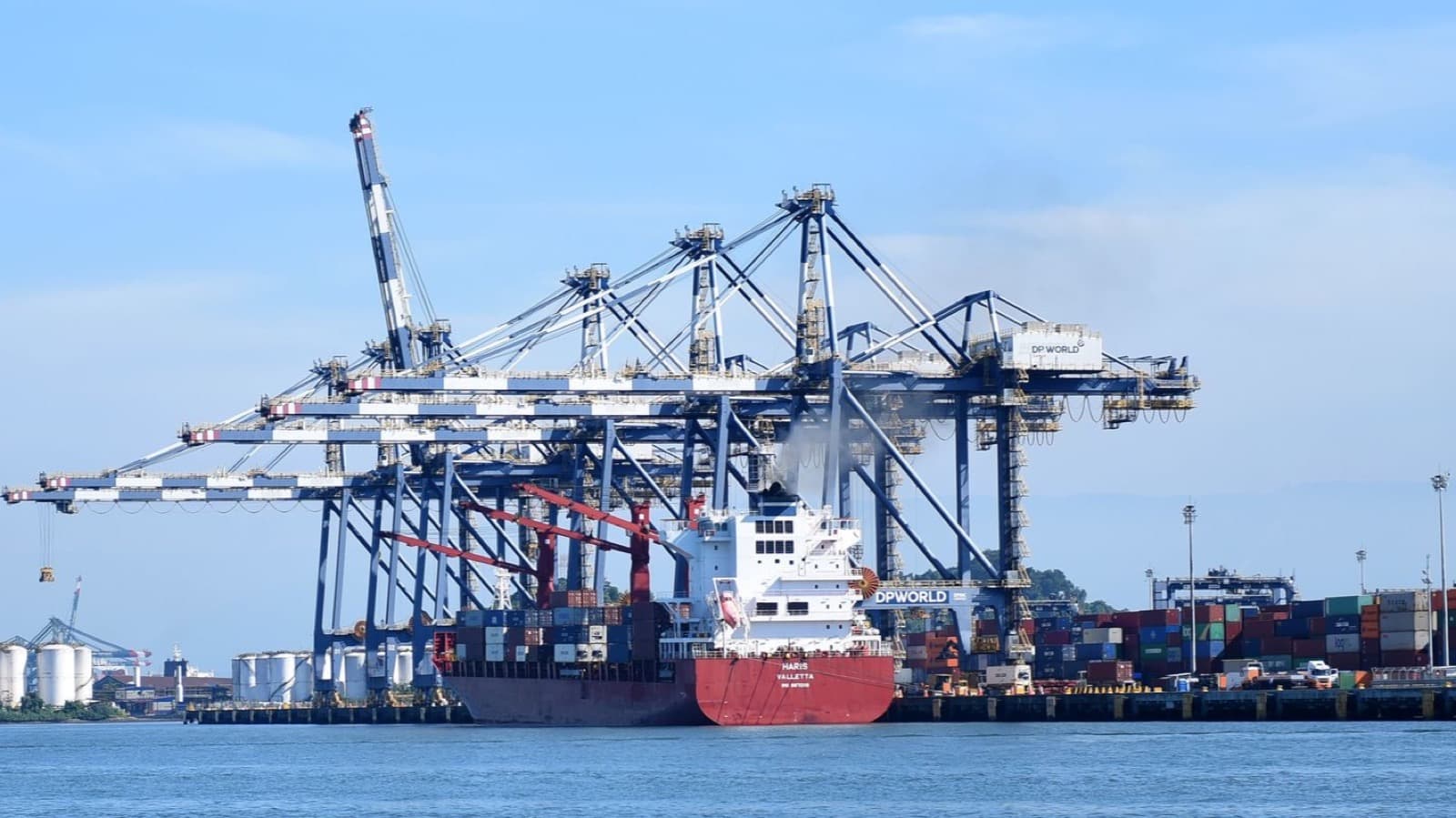 Navio porta-contêineres atracado sob guindastes portuários no Porto de Santos, com pátio de contêineres ao fundo