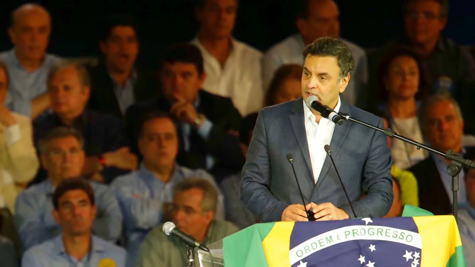 Aécio Neves discursa em convenção do PSDB, com bandeira do Brasil ao fundo