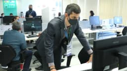 Técnico eleitoral prepara urna eletrônica em sala com computadores
