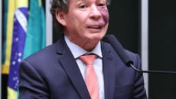 Deputado federal Reginaldo Lopes discursa na tribuna da Câmara dos Deputados com bandeira do Brasil ao fundo