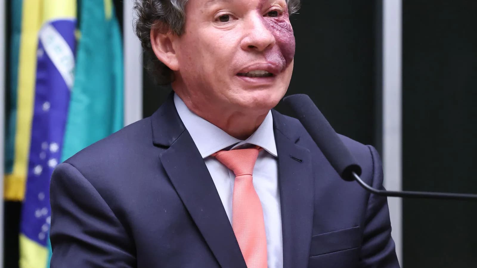 Deputado federal Reginaldo Lopes discursa na tribuna da Câmara dos Deputados com bandeira do Brasil ao fundo
