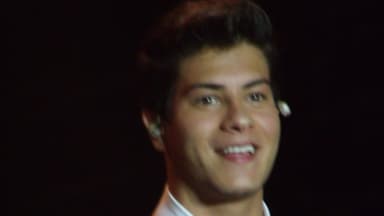 Arthur Aguiar sorri durante apresentação em show, com microfone na mão e ponto eletrônico no ouvido