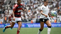 Jogadoras do Corinthians e do Flamengo disputam a bola em partida de futebol feminino, com a torcida ao fundo