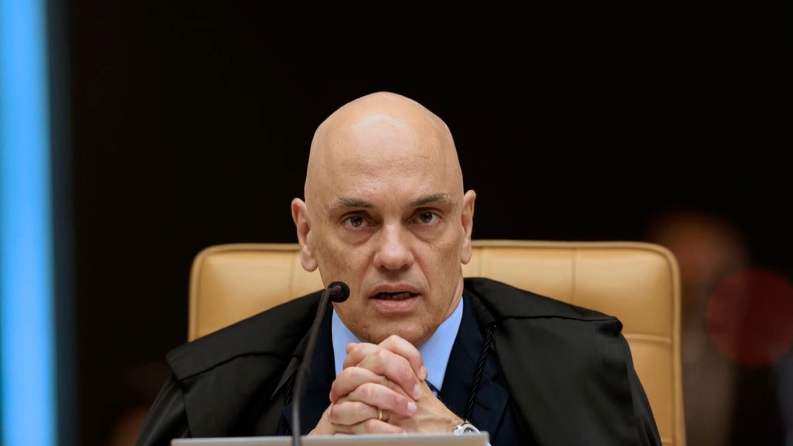 O ministro Alexandre de Moraes durante sessão plenária do STF, com as mãos entrelaçadas próximas ao microfone