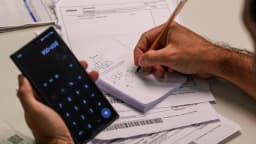 Pessoa calcula contas com celular e boletos sobre a mesa