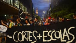 Estudantes em manifestação à noite, segurando faixa com os dizeres 'menos cortes, mais escolas' (foto de arquivo)
