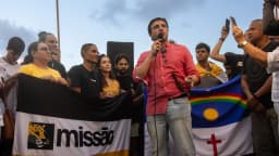 Renan Santos discursa ao microfone em ato de campanha do partido Missão, cercado por apoiadores com bandeiras