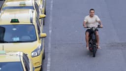 Motoboy conduz moto em via pública ao lado de táxis amarelos
