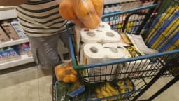 Consumidor coloca produtos em carrinho de supermercado, com prateleiras ao fundo