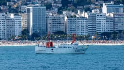 Navio oceanográfico da Marinha do Brasil navegando próximo à orla do Rio de Janeiro, com prédios ao fundo