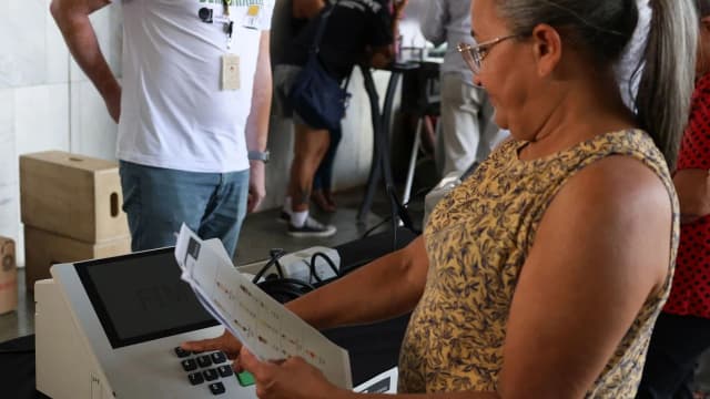 Eleitora segura cola eleitoral enquanto usa urna eletrônica em seção de votação