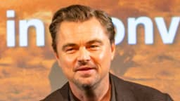 Leonardo DiCaprio sorri em evento público, vestindo blazer, com painel ao fundo (foto de arquivo)
