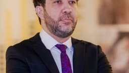 André Janones, de terno escuro e gravata estampada, posa de braços cruzados