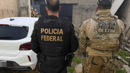 Dois agentes da Polícia Federal, de costas, ao lado de viatura durante operação contra tráfico de armas