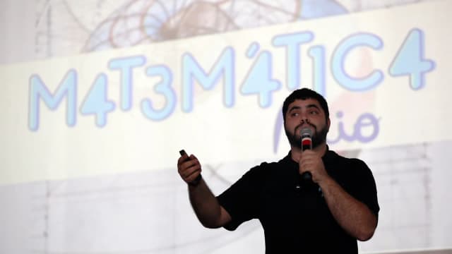 Professor dá aula preparatória com apresentação de matemática projetada ao fundo, cena ilustrativa de preparação para concurso