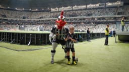 Mascote Galo Doido do Atlético-MG ao lado de um torcedor no gramado