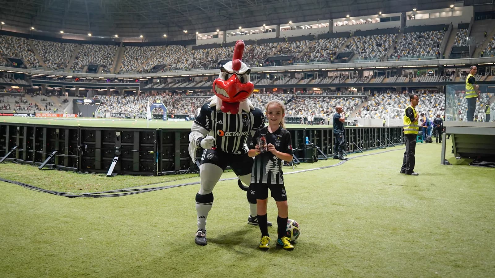 Mascote Galo Doido do Atlético-MG ao lado de um torcedor no gramado