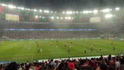 Torcedores do Flamengo acompanham jogo no Maracanã lotado, com o time em campo ao fundo