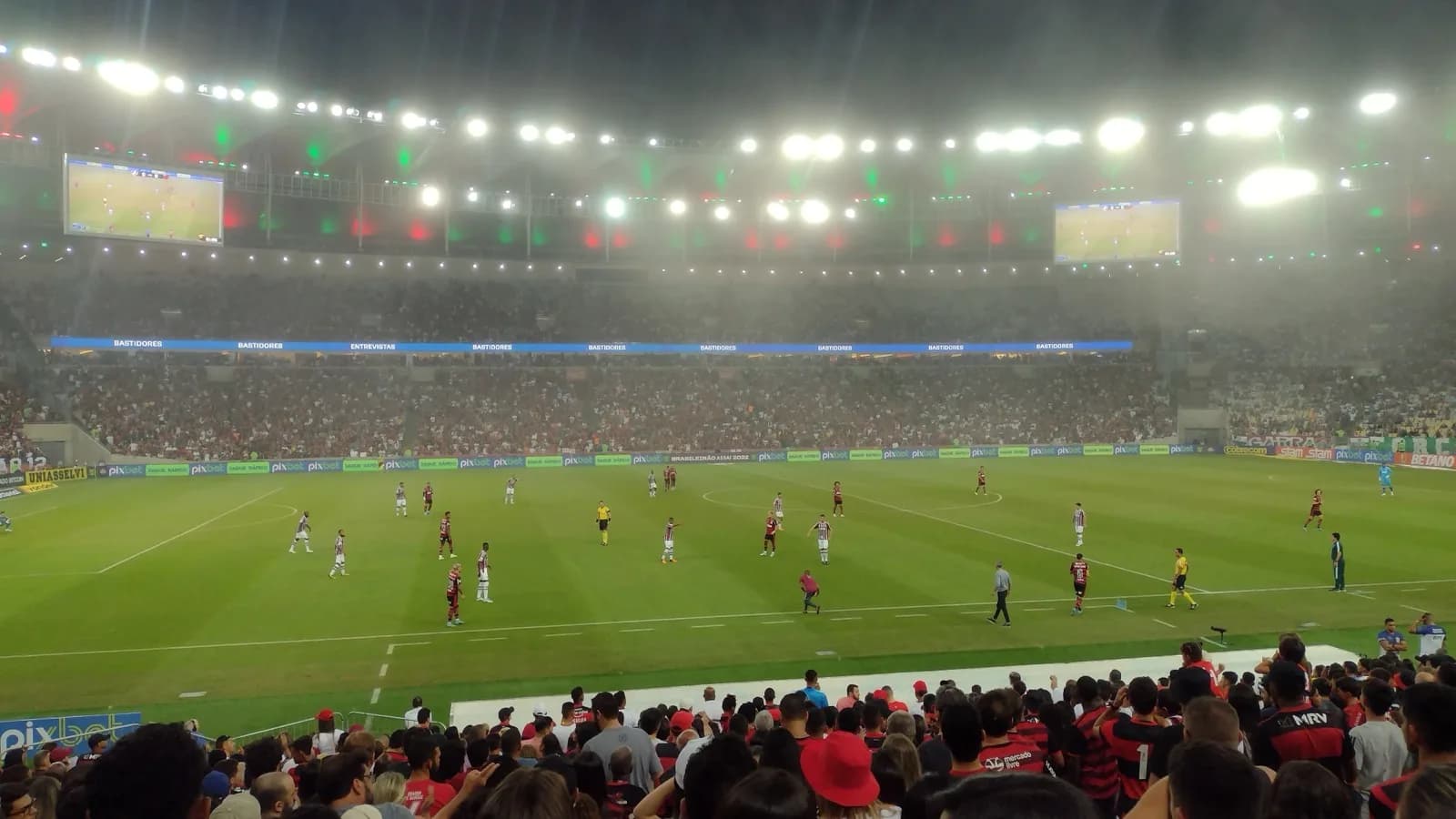 Torcedores do Flamengo acompanham jogo no Maracanã lotado, com o time em campo ao fundo