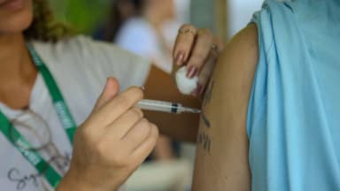 Profissional de saúde aplica vacina no braço de uma pessoa em posto de vacinação