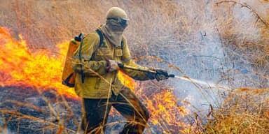 Brigadista do ICMBio combate incêndio em vegetação seca com jato d'água (foto de arquivo)