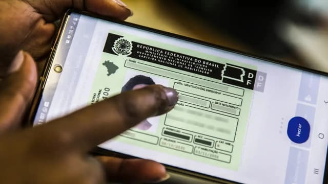 Mão segura celular com a Carteira Nacional de Habilitação aberta no aplicativo CNH Digital