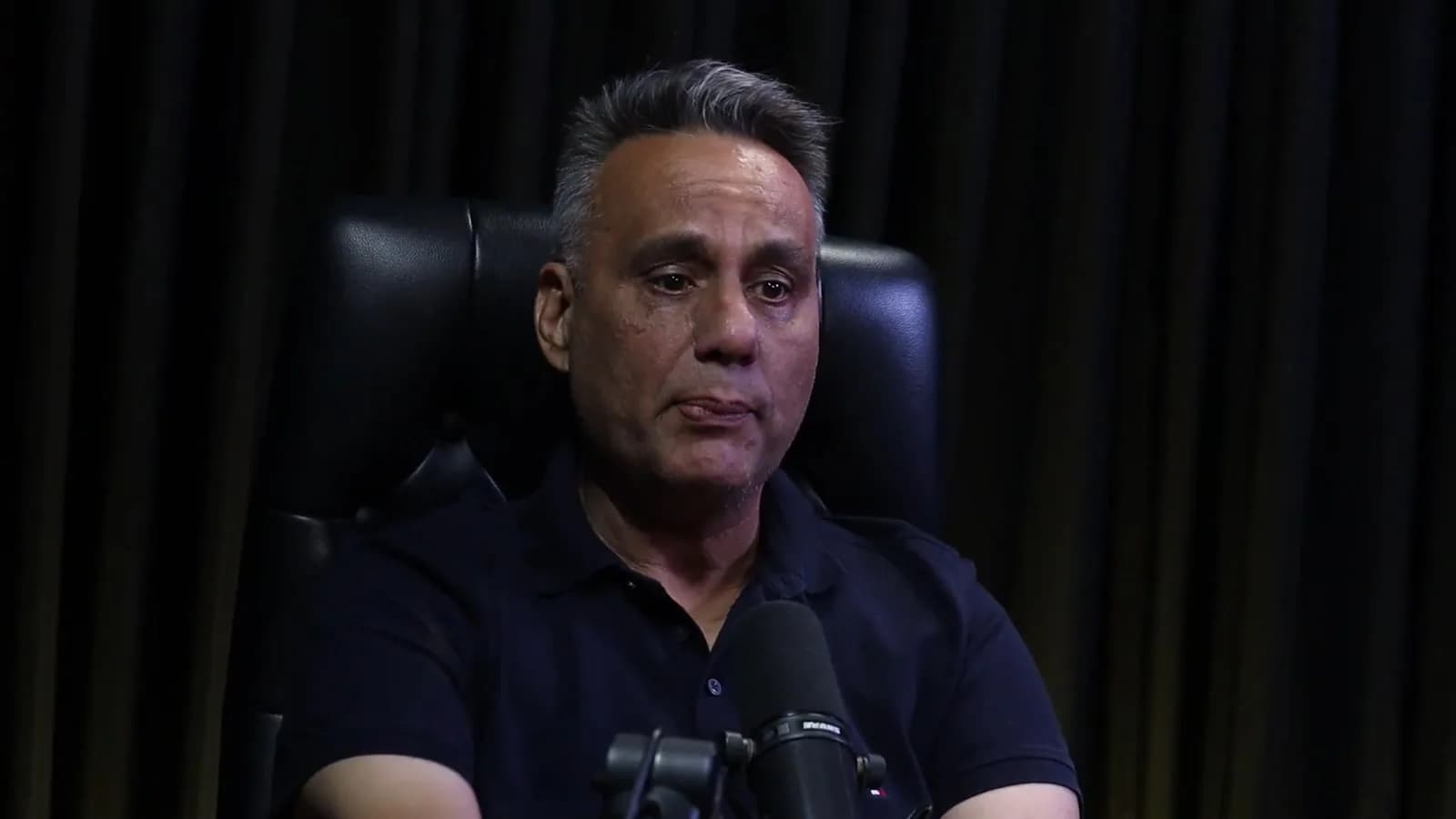 Rogério Furtado fala durante o podcast Encampus, em cadeira de couro preta contra fundo de cortina escura